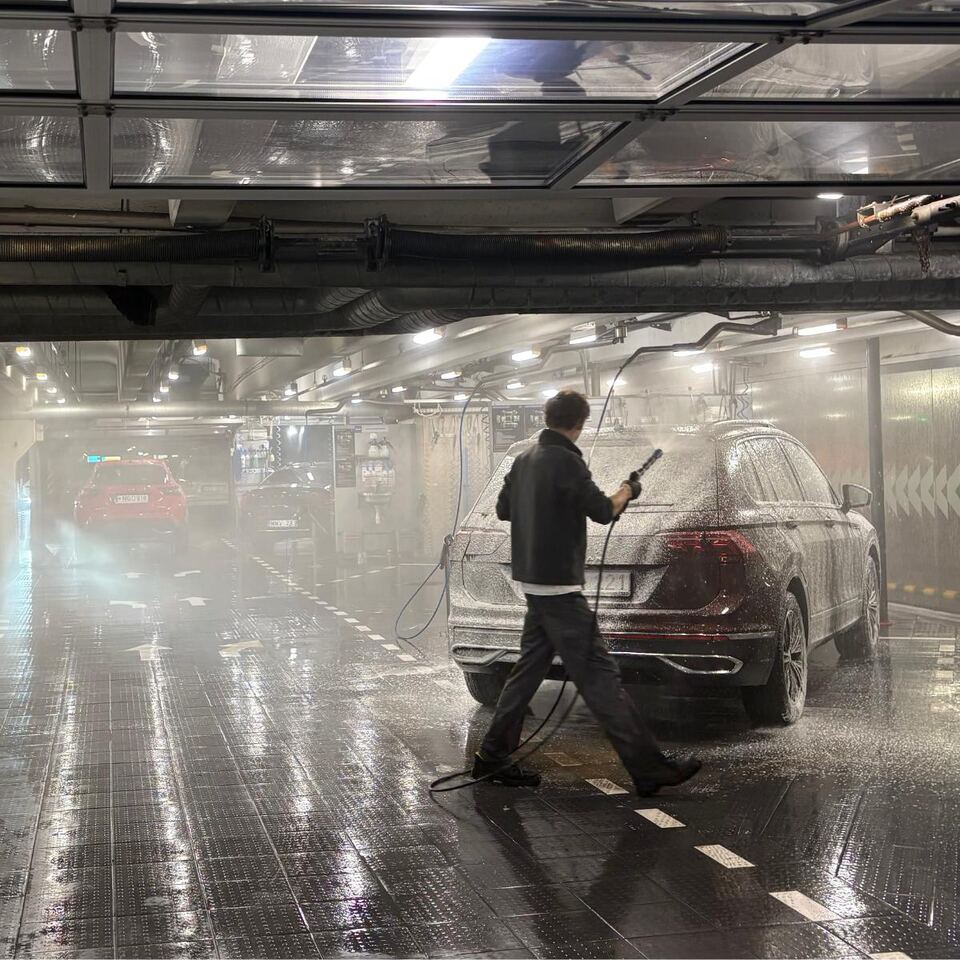 A HOCUS staff member pressure-washing a maroon SUV by hand in an underground HOCUS wash bay in Vilnius, Lithuania