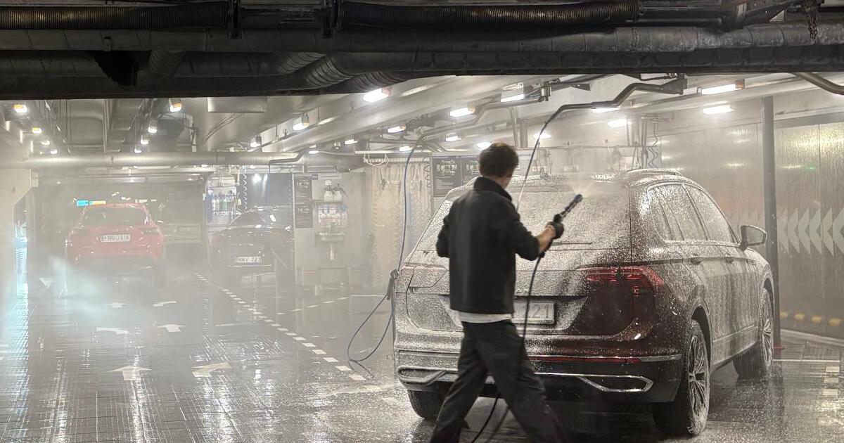 A HOCUS staff member pressure-washing a maroon SUV by hand in a HOCUS wash bay in Vilnius, Lithuania